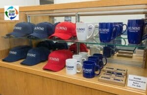 How Toyota Used a Pull System in a NUMMI Gift Shop Red and navy baseball caps with "NUMMI" embroidered, along with white and blue mugs, pens, and a display shelf.