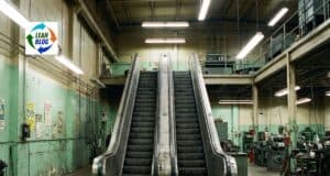 Escalator in an industrial workshop setting with machinery and green walls.