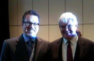 Meeting Newt Gingrich, a Lean Champion Two men stand side by side, smiling at the camera. Both are dressed in suits, with the man on the left wearing glasses and a blue tie, and the man on the right also wearing glasses and a darker suit with a red tie. The background is dimly lit and the image is slightly dark. lean blog