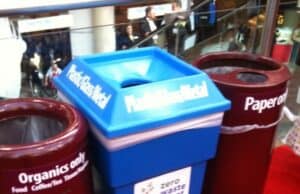 What's the Point of Standard if it's Not Followed? Three waste bins are positioned side by side on a red carpet. The left bin is brown for "Organics only," the middle bin is blue for "Plastic, Glass, Metal," and the right bin is brown for "Paper only." A sign on the middle bin reads "Zero Waste Event. lean blog