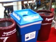 What's the Point of Standard if it's Not Followed? Three waste bins are positioned side by side on a red carpet. The left bin is brown for "Organics only," the middle bin is blue for "Plastic, Glass, Metal," and the right bin is brown for "Paper only." A sign on the middle bin reads "Zero Waste Event. lean blog