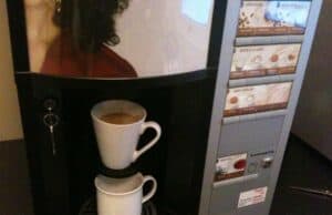 A Coffee Machine that’s Mistake Proofed A coffee vending machine is dispensing coffee into two white mugs stacked on top of each other. The machine has a panel displaying options for different types of coffee beverages, and a small slot with a key on the left side. lean blog