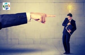 Leadership Without Blame: Building Psychological Safety in the New Year arm and finger of a workplace boss pointing a finger of blame at an employee who looks scared to share their idea.