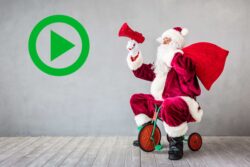 Play button icon next to Santa riding a tricycle with a large red sack, against a plain wall background.