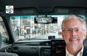 “Toyota Culture” 20 Years Later: Why Liker’s Lessons Still Matter in 2026 Rainy city street viewed from a taxi cab with a smiling man in the foreground.