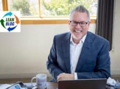 A Brief Response From Mark (The Human) Mark Graban smiling at his desk with a laptop and My Favorite Mistake coffee mug, apparently unbothered by his AI's public meltdown