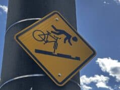 Warning: Signs! Mistake-Proofing Is More Effective Than Warnings Yellow diamond warning sign on a pole showing a cyclist flying over handlebars after hitting streetcar tracks, along the Ohio River in Cincinnati