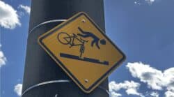 Yellow diamond warning sign on a pole showing a cyclist flying over handlebars after hitting streetcar tracks, along the Ohio River in Cincinnati