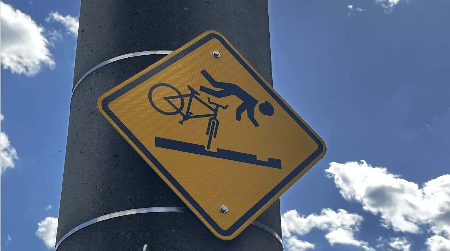 Yellow diamond warning sign on a pole showing a cyclist flying over handlebars after hitting streetcar tracks, along the Ohio River in Cincinnati