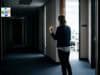 What Can a CI Director Do When Executives Undermine Psychological Safety? Person hesitating in a corporate hallway outside an open office door with bright fluorescent light spilling through the doorway.