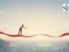 Even in Japan: A Target of Zero and a Process That Lives Near Seven Percent Manga- and anime-influenced editorial illustration in a wide horizontal format. A small lone figure, seen from behind in plain clothes, stands on a glowing crimson ribbon that stretches horizontally across the frame like a floating path. The ribbon gently rises and falls but stays level. The person leans forward with one arm extended, reaching toward a soft sage-green glowing ring far below and ahead across a wide empty gap. Pale cliffs frame the distant lower edges, while most of the image is filled with a vast cream-to-blue sky with thin clouds and ample negative space. The mood is quiet, reflective, and slightly wistful.