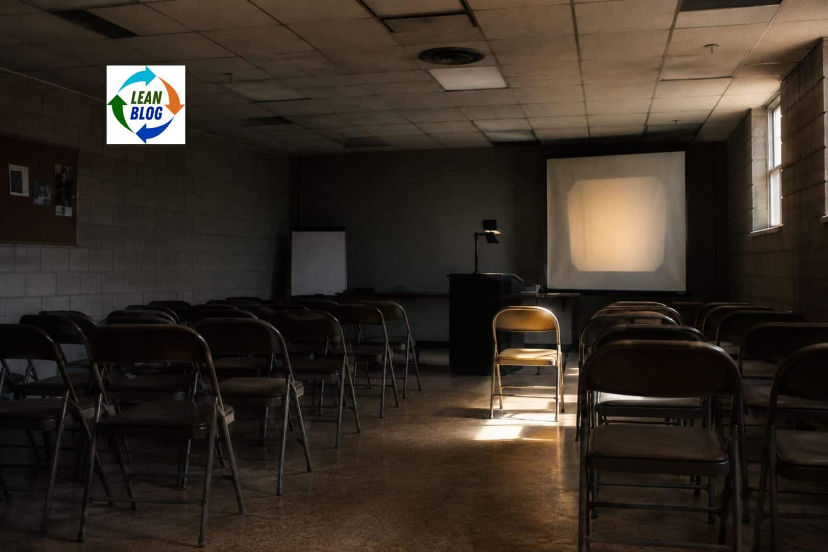 Empty seminar room with folding chairs and an overhead projector, one chair lit by window light