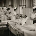 Historical black-and-white image of nurses and aides performing separate tasks for patients in a crowded hospital ward, illustrating functional or assembly-line nursing.