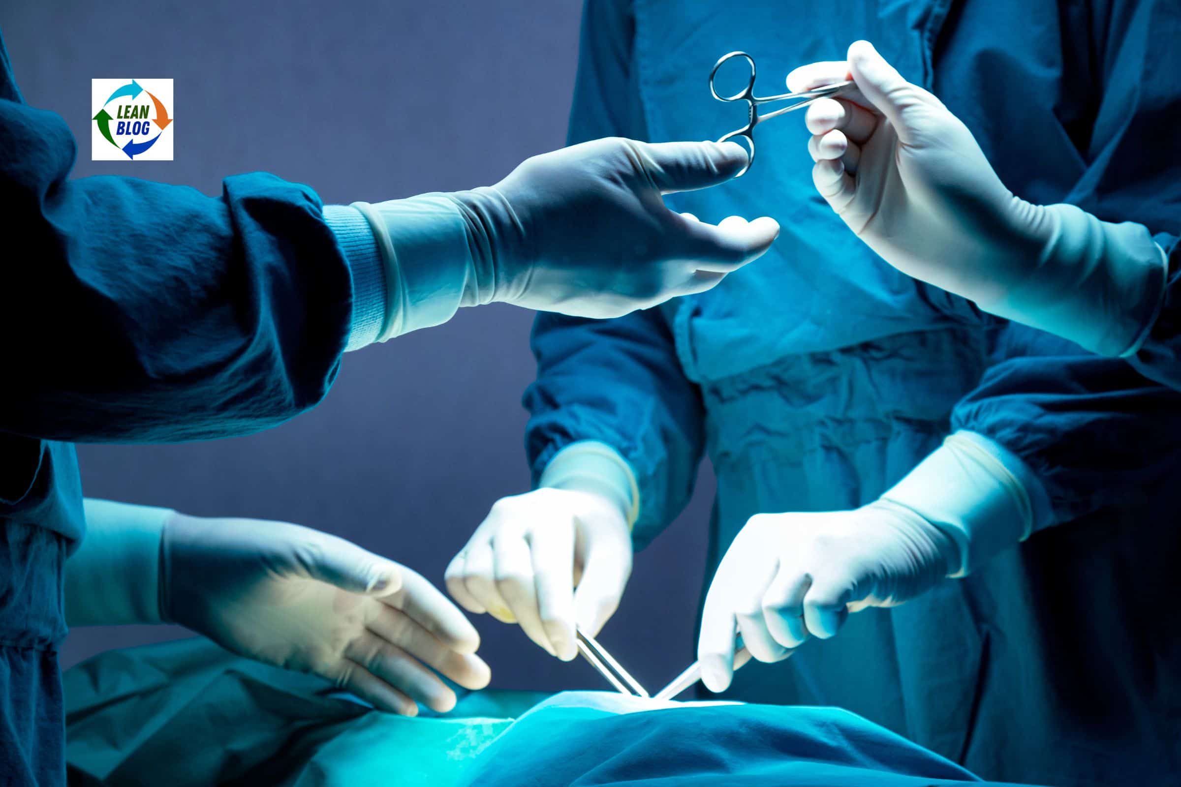 Medical personnel in blue scrubs and gloves performing surgery, passing a surgical instrument in a sterile environment