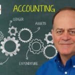 Nick Katko in blue shirt beside chalkboard reading ACCOUNTING with chalk gears labeled Payable, Ledger, Assets, Expenditure, Review